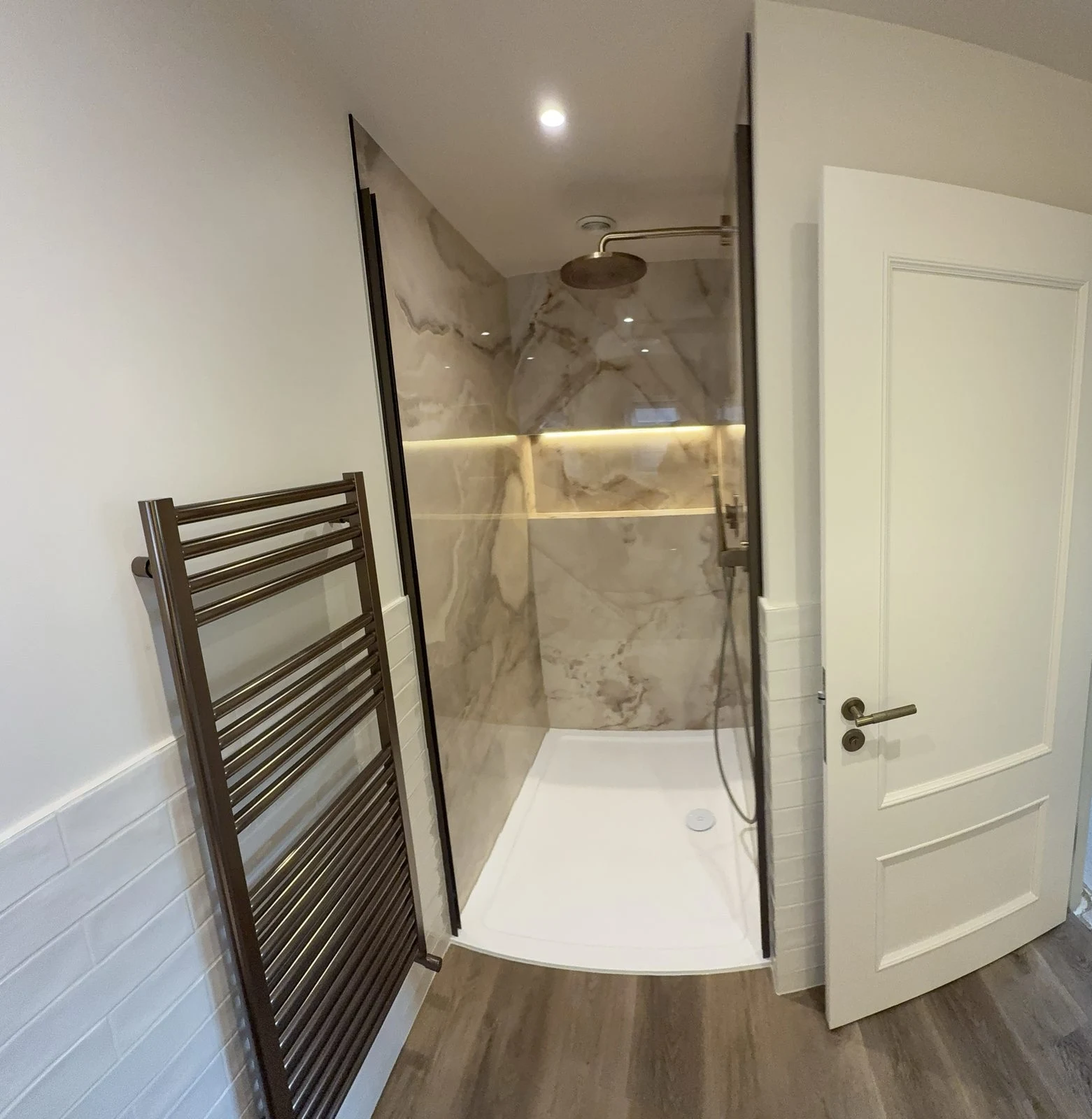 Walk-in shower with large-format onyx-effect porcelain, brushed bronze rainfall shower and LED-lit niche in Bath