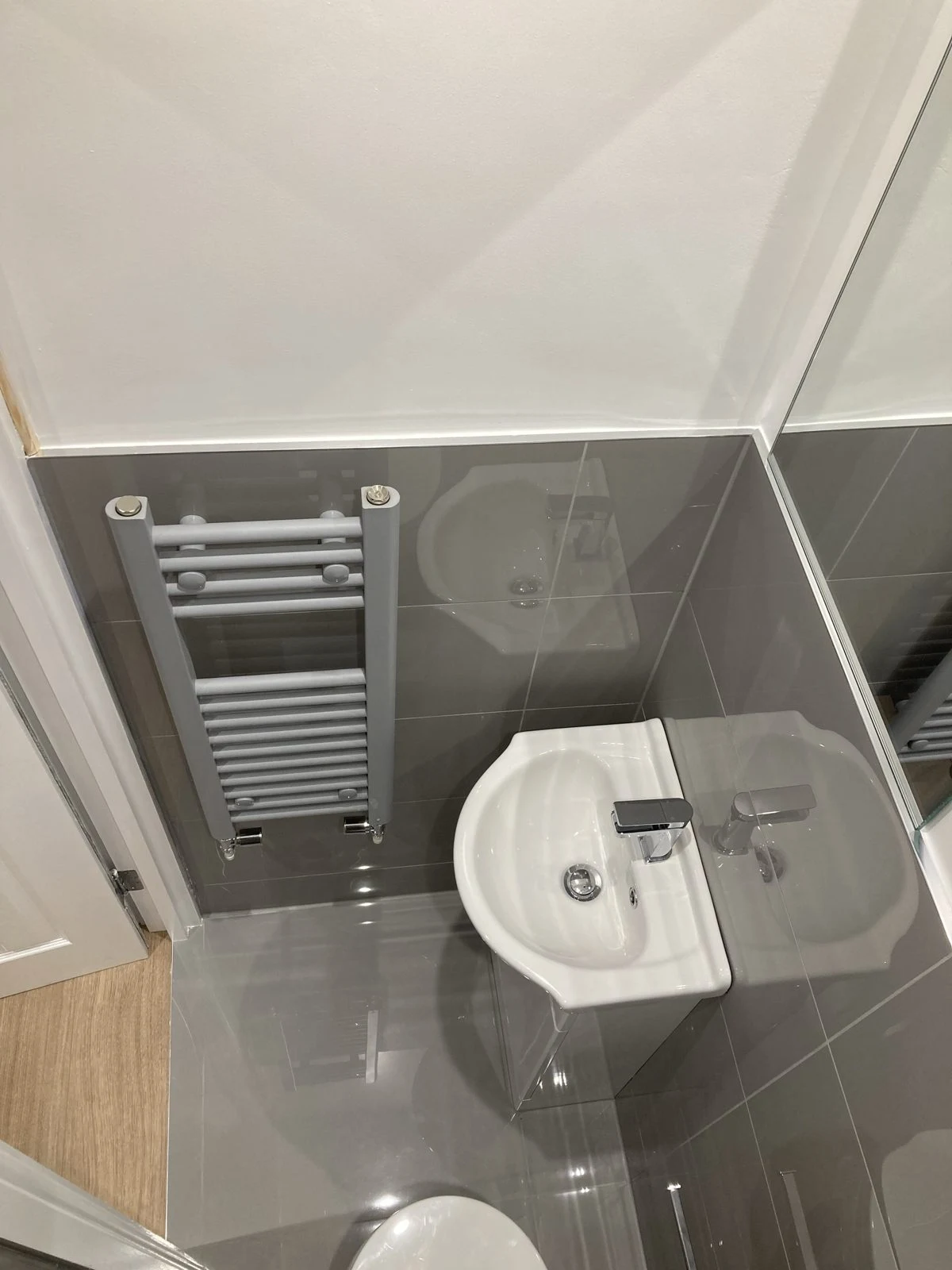 Cloakroom with grey gloss tiles, compact basin and towel radiator