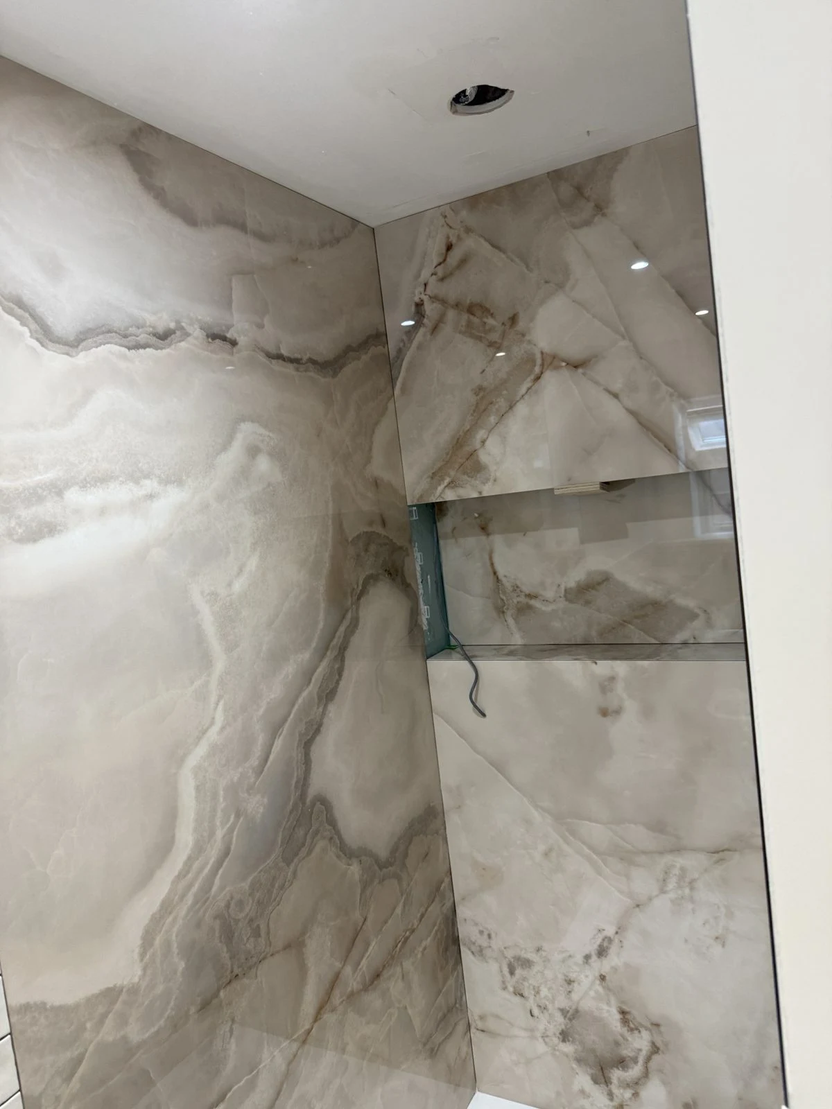 Large-format onyx-effect porcelain being fitted in a shower enclosure in Bath
