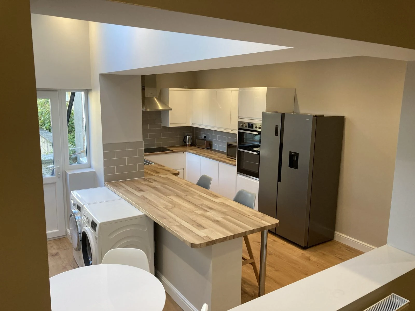 White gloss handleless kitchen with oak-effect breakfast bar and grey metro tile splashback