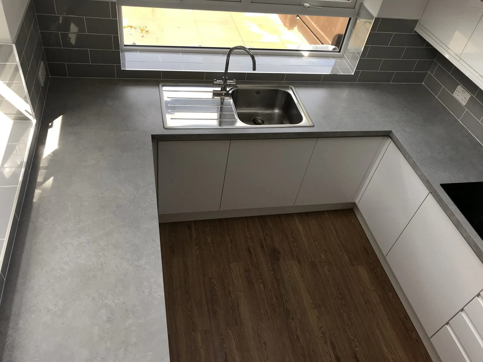 Stainless steel sink under a window with stone-effect worktop and grey metro tiles