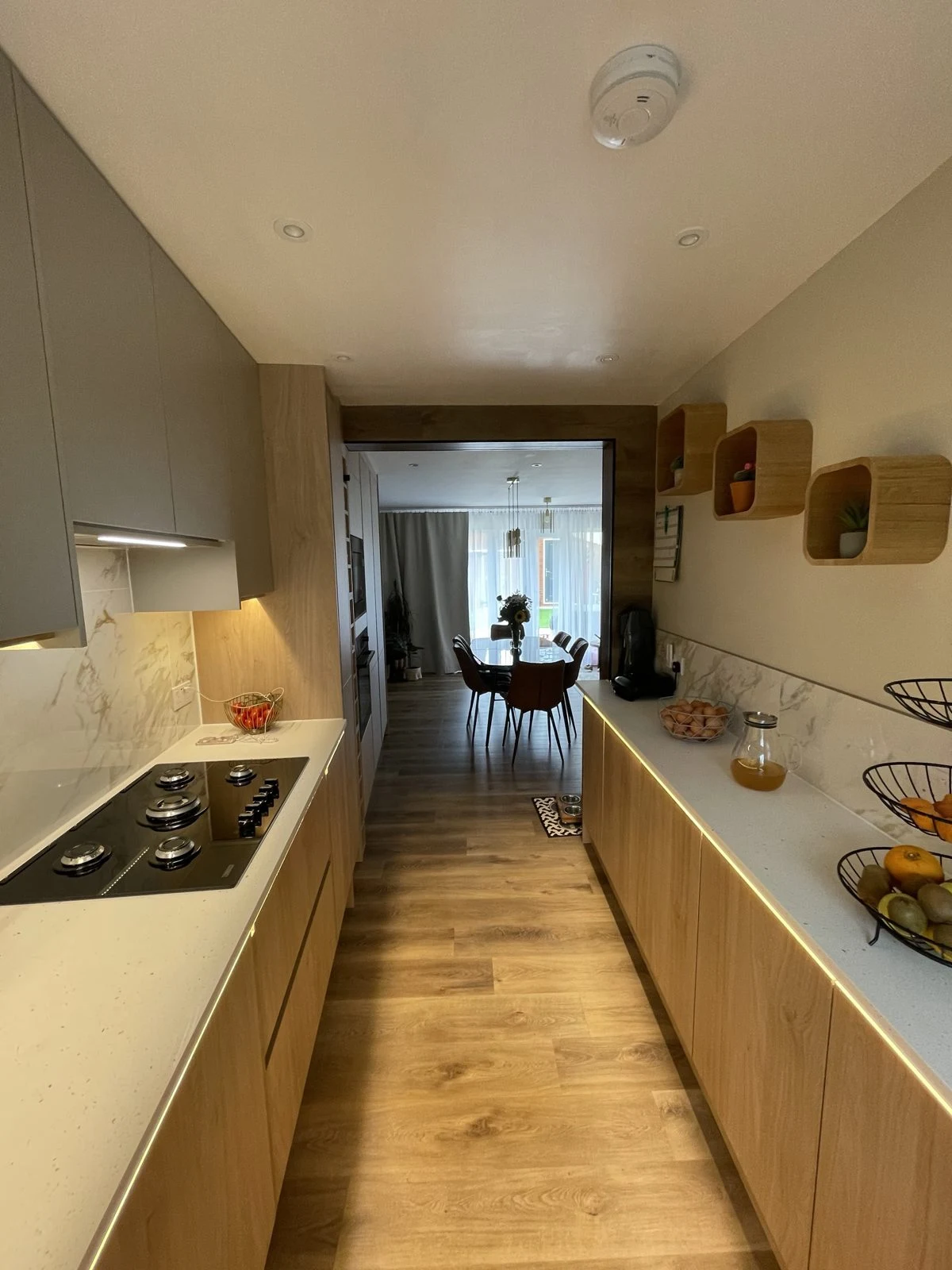Galley kitchen renovation with oak-effect handleless units, white quartz worktops and LED lighting under the worktops