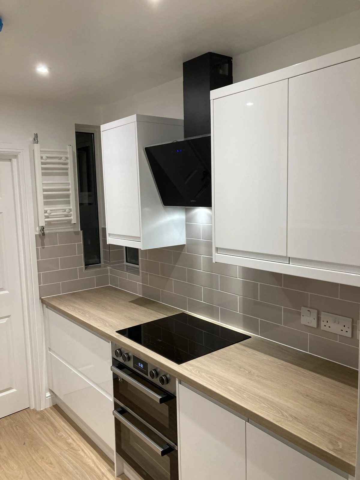 White gloss kitchen with induction hob, black angled cooker hood and oak-effect worktop
