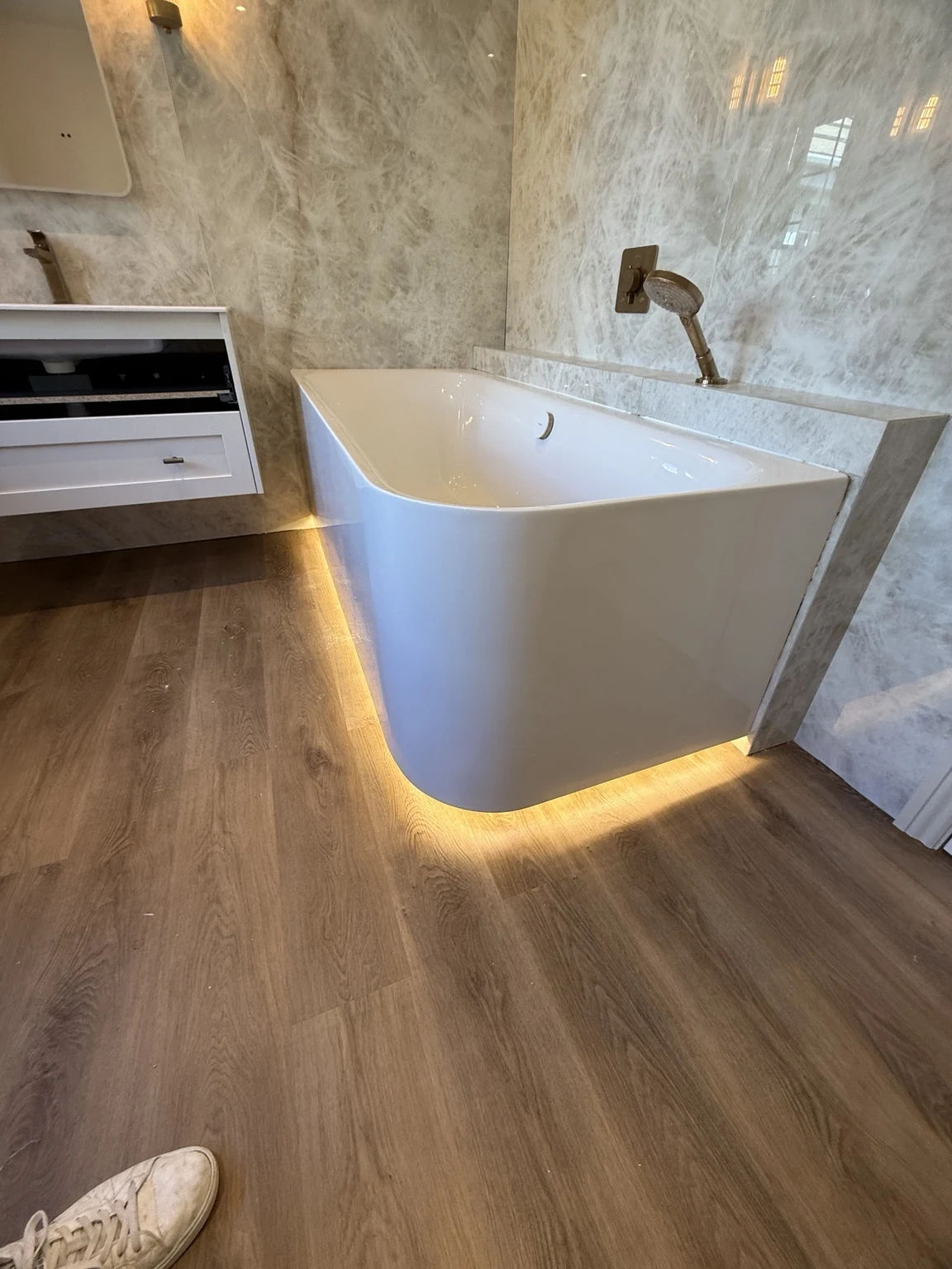 Completed bathroom in Swindon with marble-effect wall tiles, a bathtub with warm underlighting and a floating vanity.