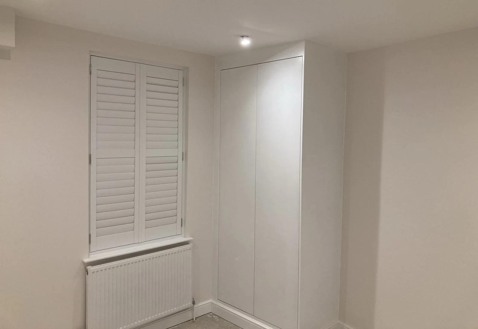 Handleless white fitted wardrobe next to plantation shutters