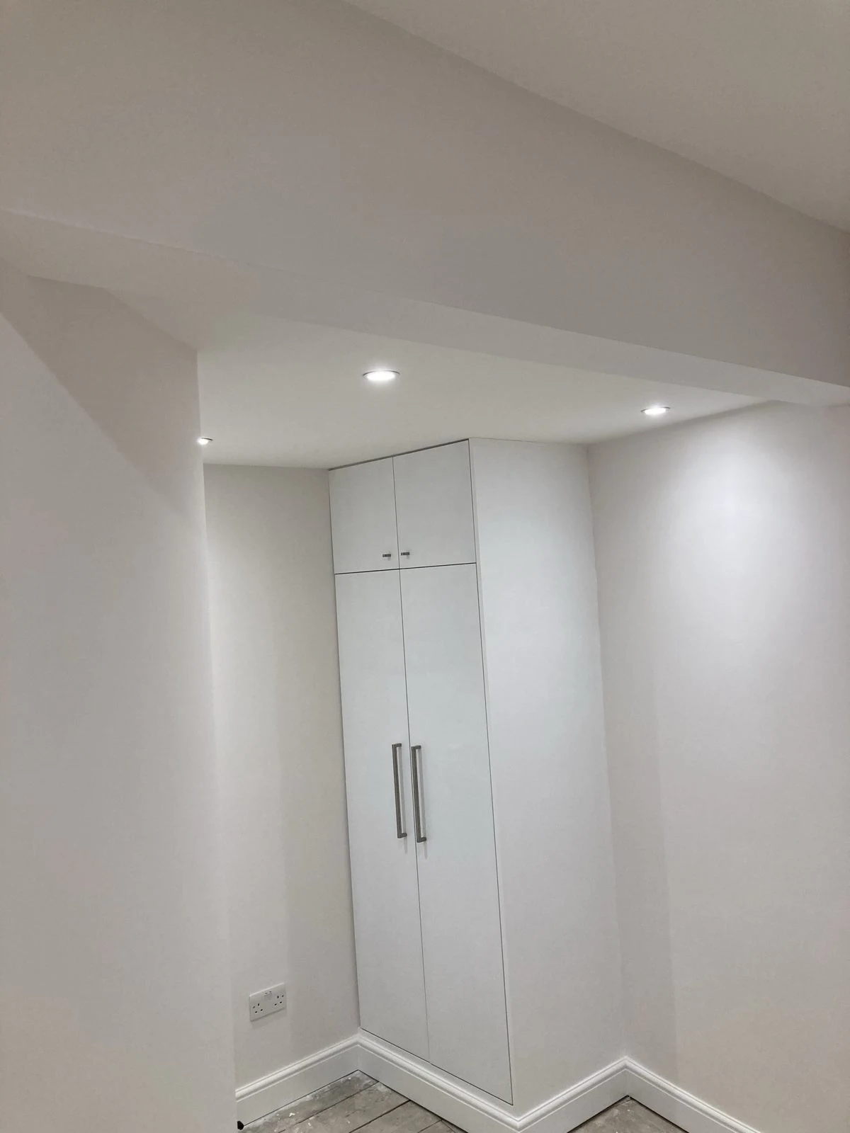 Tall white fitted wardrobe with top cupboards and bar handles